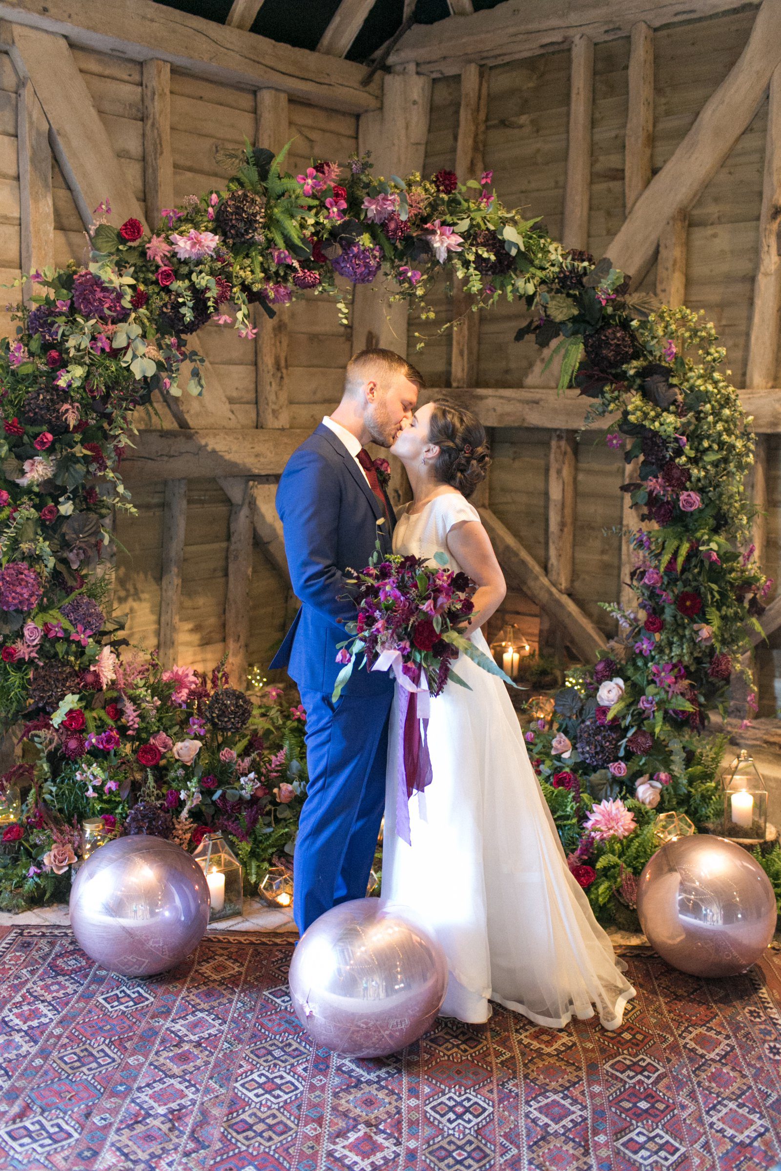 Bride and groom kissing in front of a floral moongate arch at High Billinghurst Farm